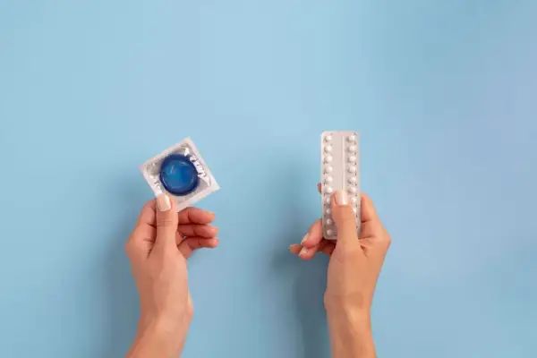 Manos sostienen un preservativo y pastillas anticonceptivas, mostrando opciones de planificación familiar.